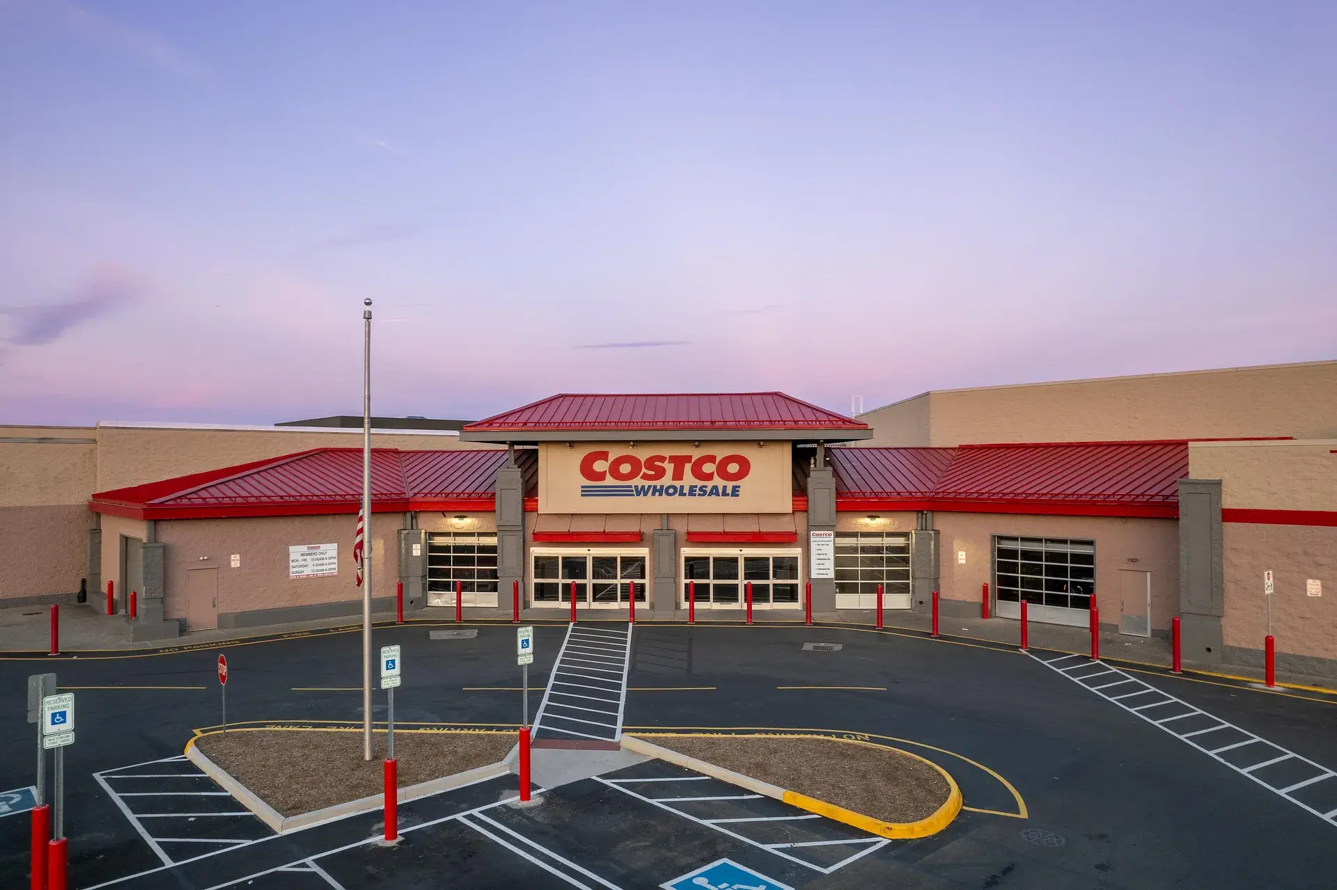 A Costco Wholesale warehouse at dusk, its red roofline and sign above the entrance and an empty parking lot in front