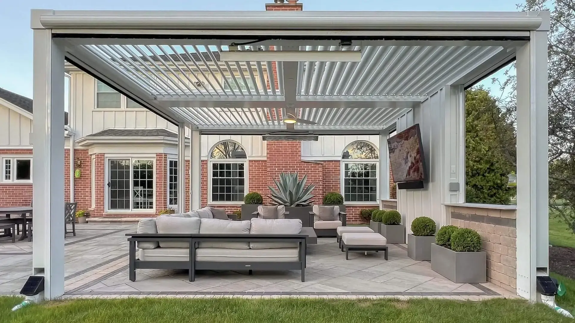 White StruXure Pergola X with its louvers open over a patio seating area beside a brick house