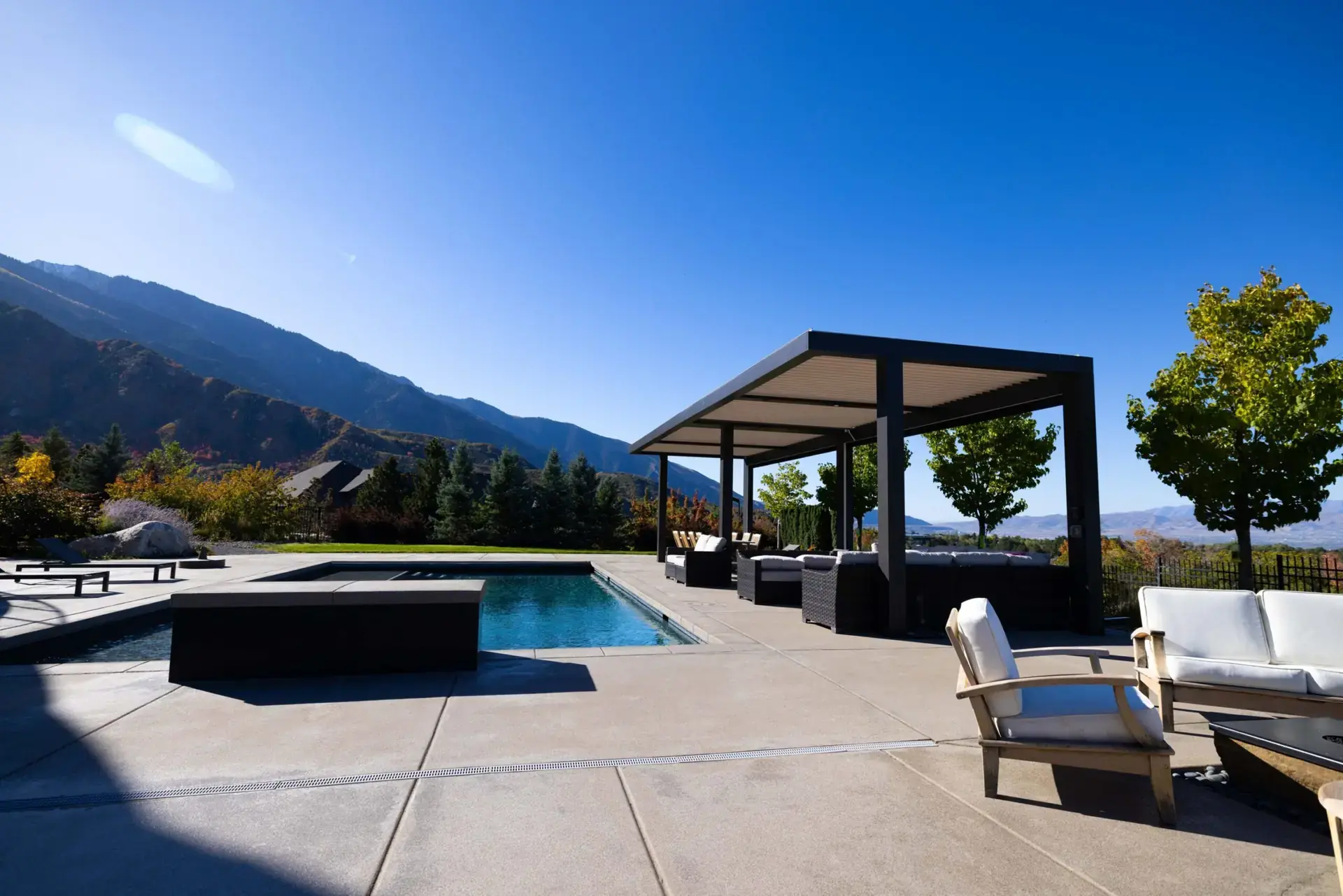 Dark freestanding StruXure Pergola X beside a swimming pool with mountains behind