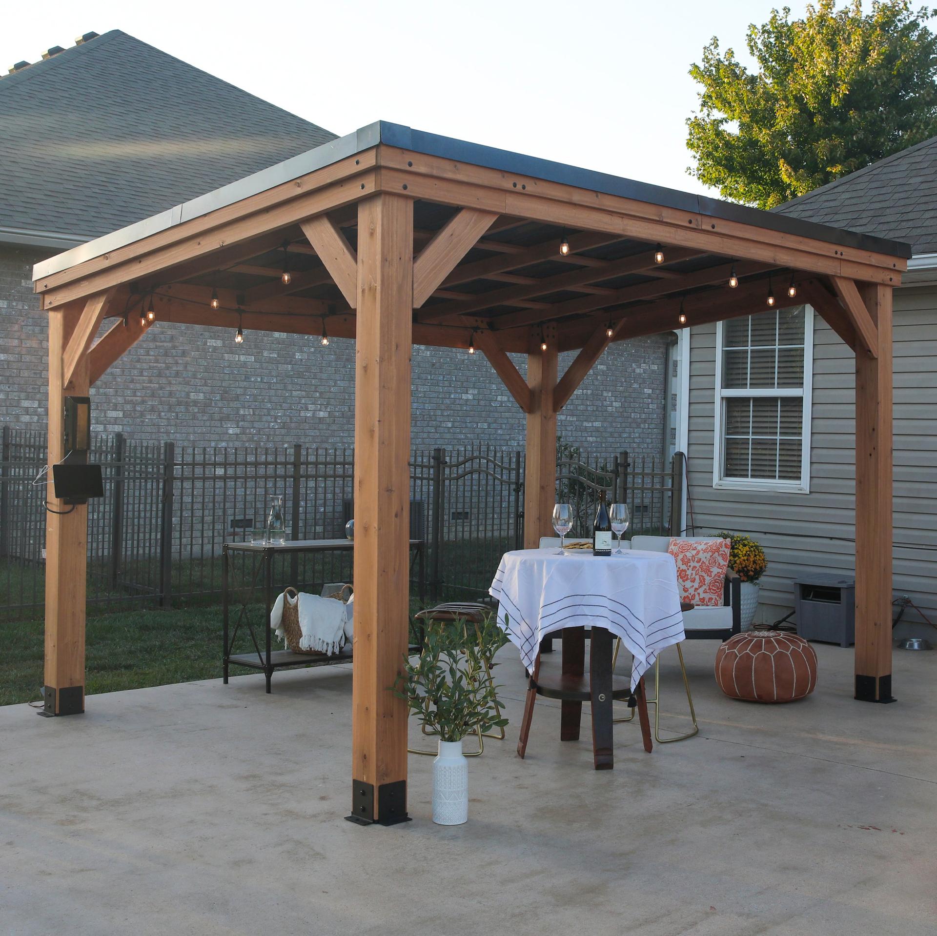 Backyard Discovery Arcadia cedar gazebo with a sloped steel roof beside a house, set with a round dining table