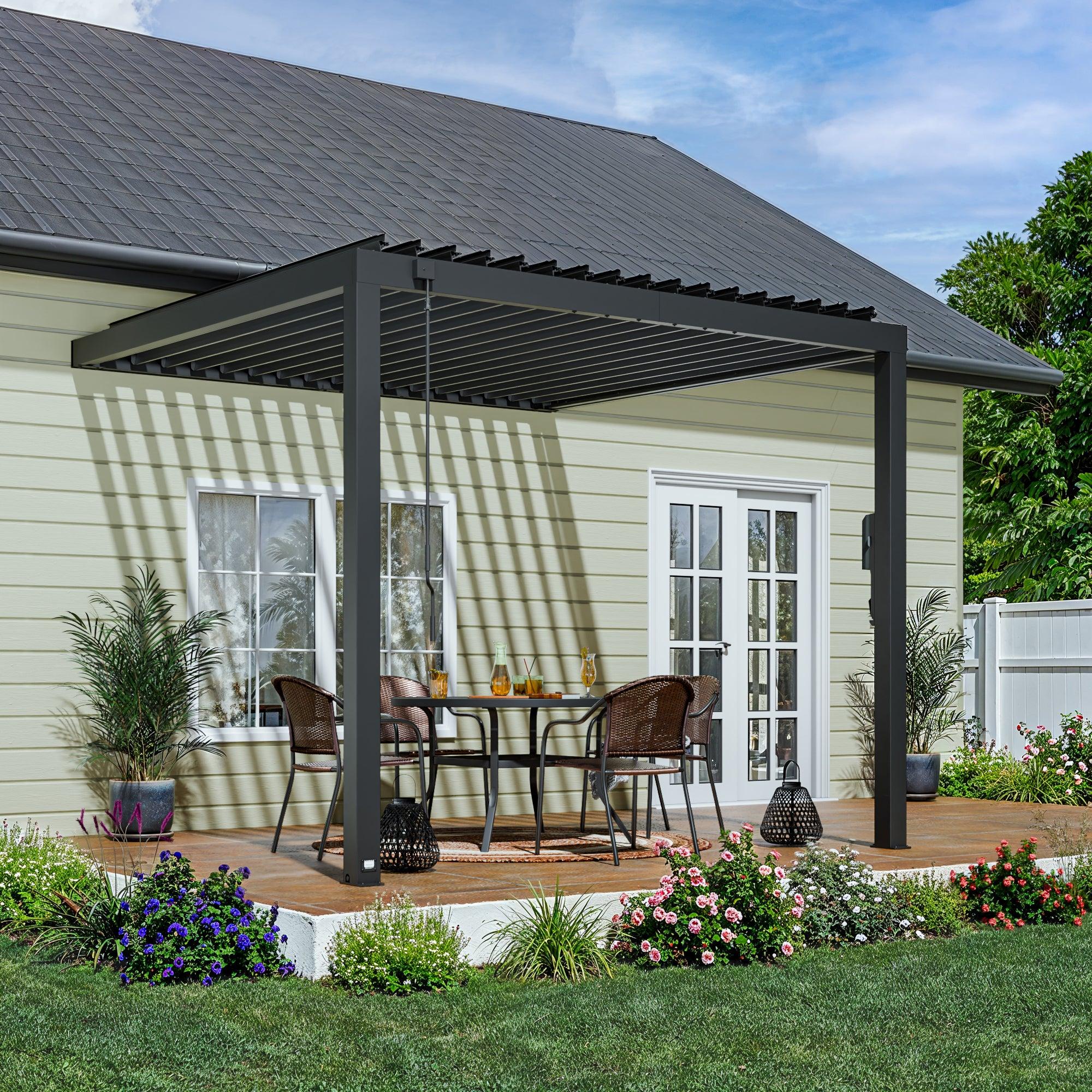 Backyard Discovery Evanston wall-mounted louvered pergola in black fixed to a cream clapboard house over a patio dining set