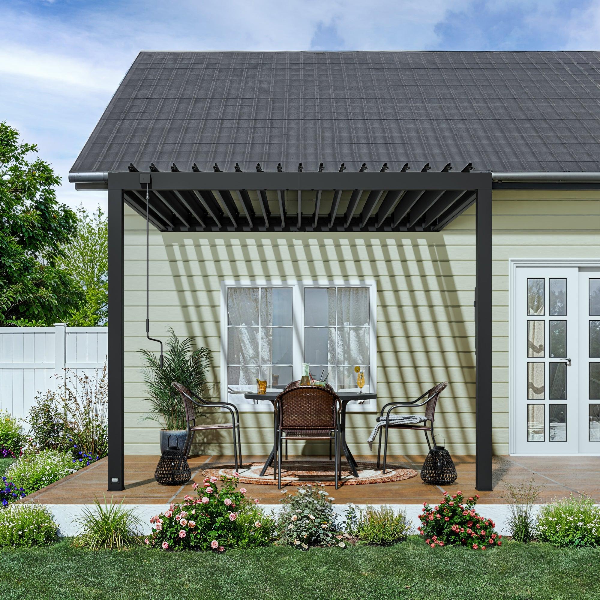 Front view of the black Evanston louvered pergola attached to the wall of a house, louvers open above a small patio table