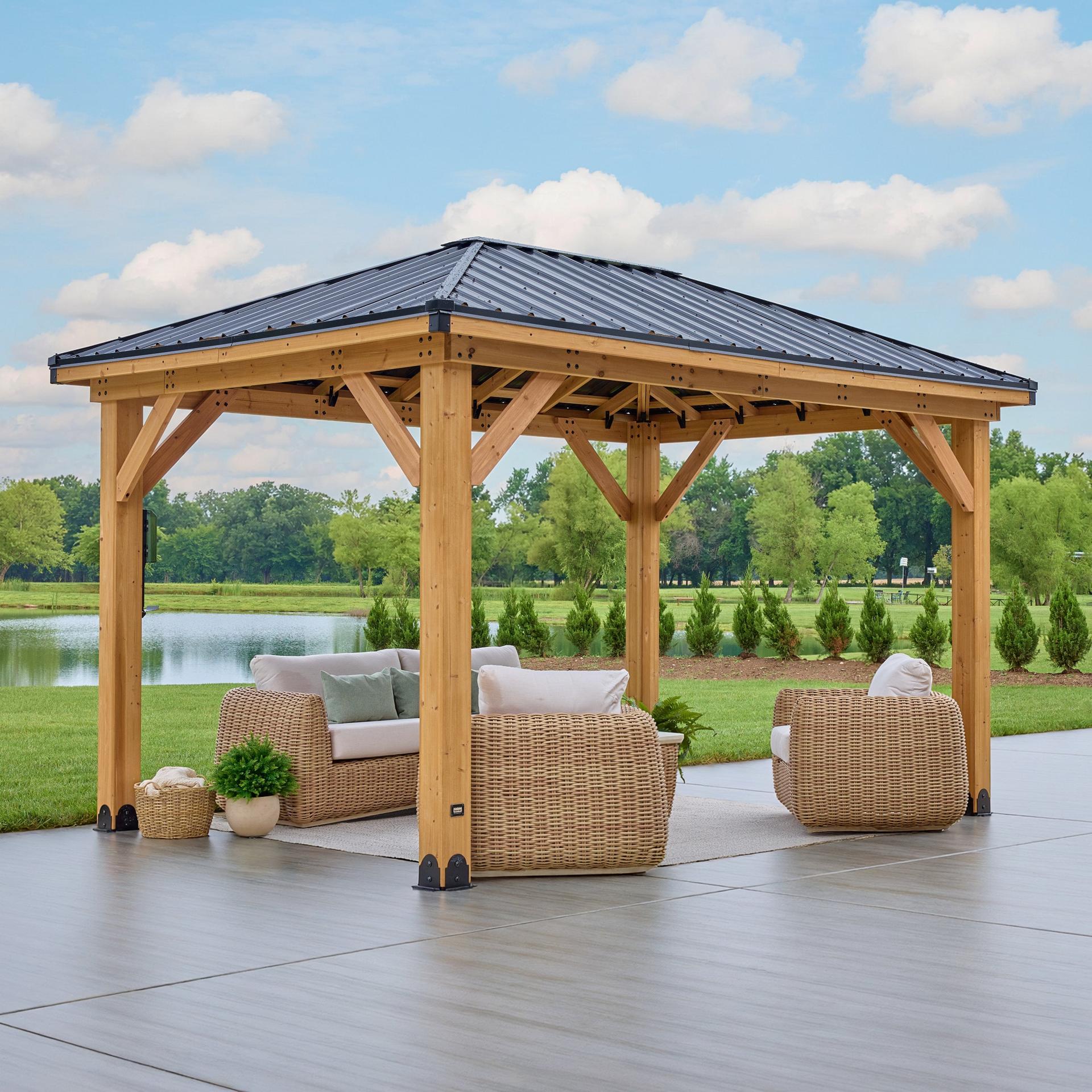 Backyard Discovery Glenmore cedar gazebo with a black steel hip roof beside a pond, set with wicker seating