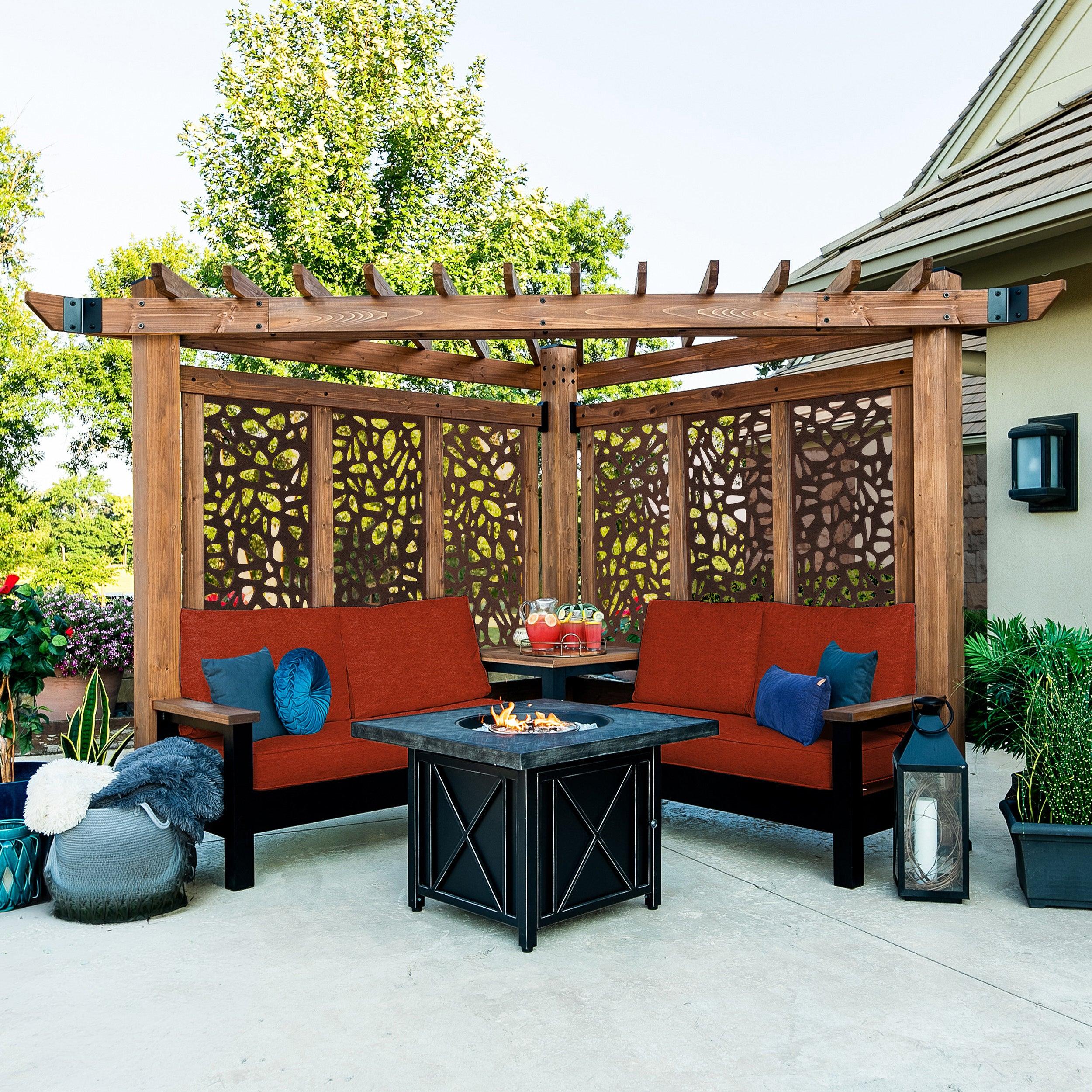 Backyard Discovery Tuscany corner pergola in cedar with pebble-pattern privacy panels, integrated sofas with orange cushions and a fire table on a patio
