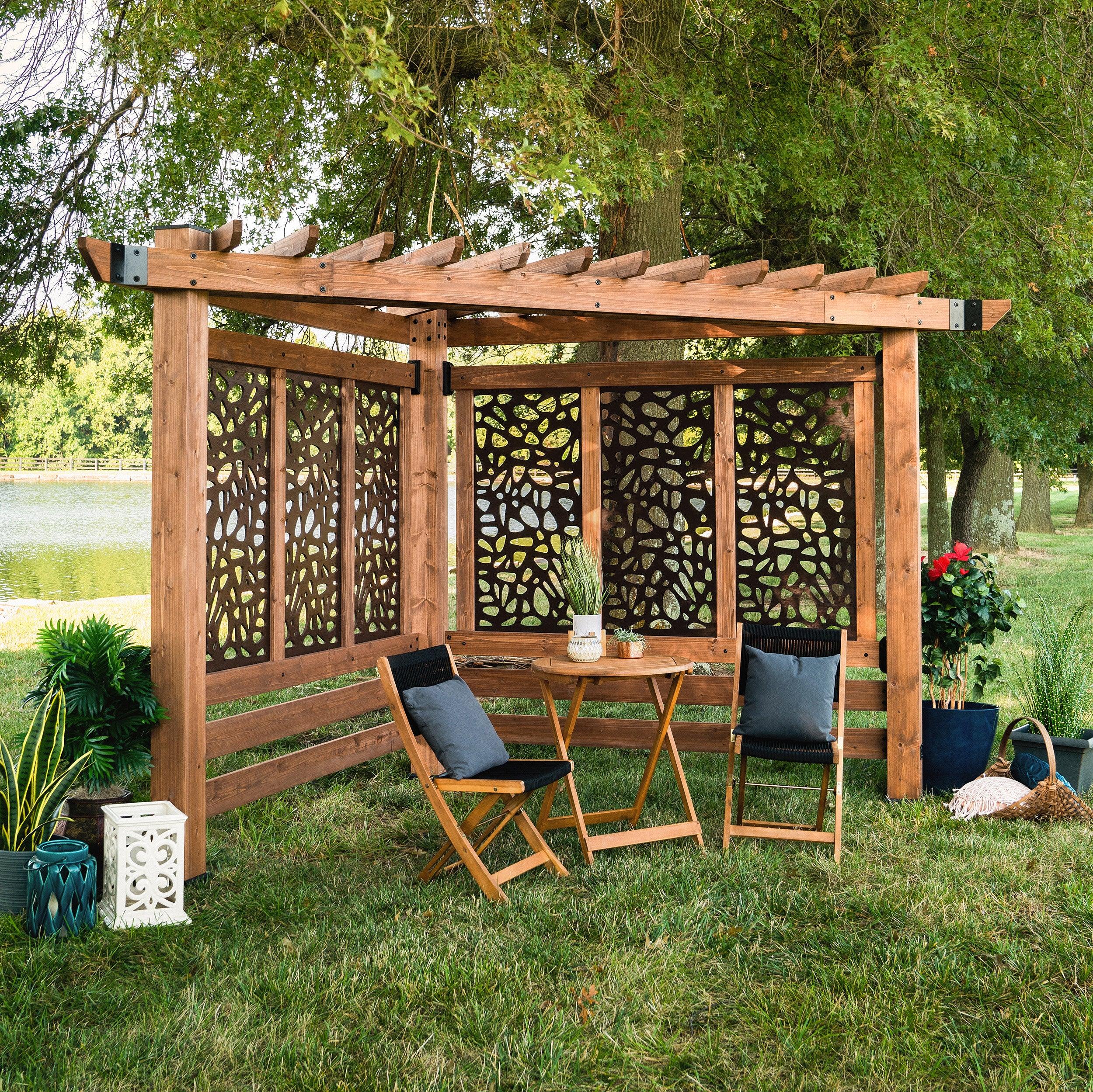 Backyard Discovery Verona corner pergola in light brown cedar with pebble-pattern composite privacy panels, set on a lawn by a lake