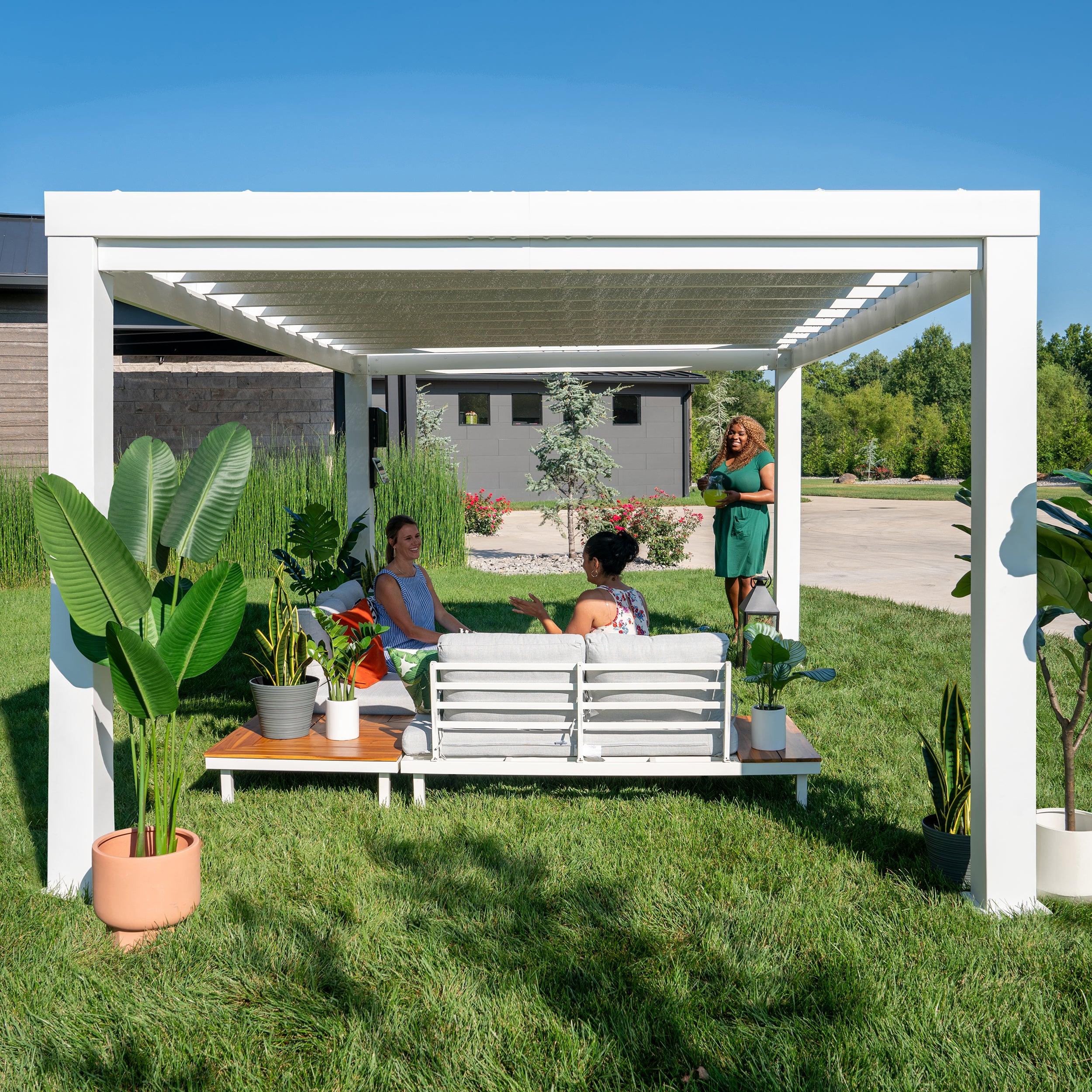 Three people talking under the white Windham steel pergola on a lawn, canopy shading the seating below