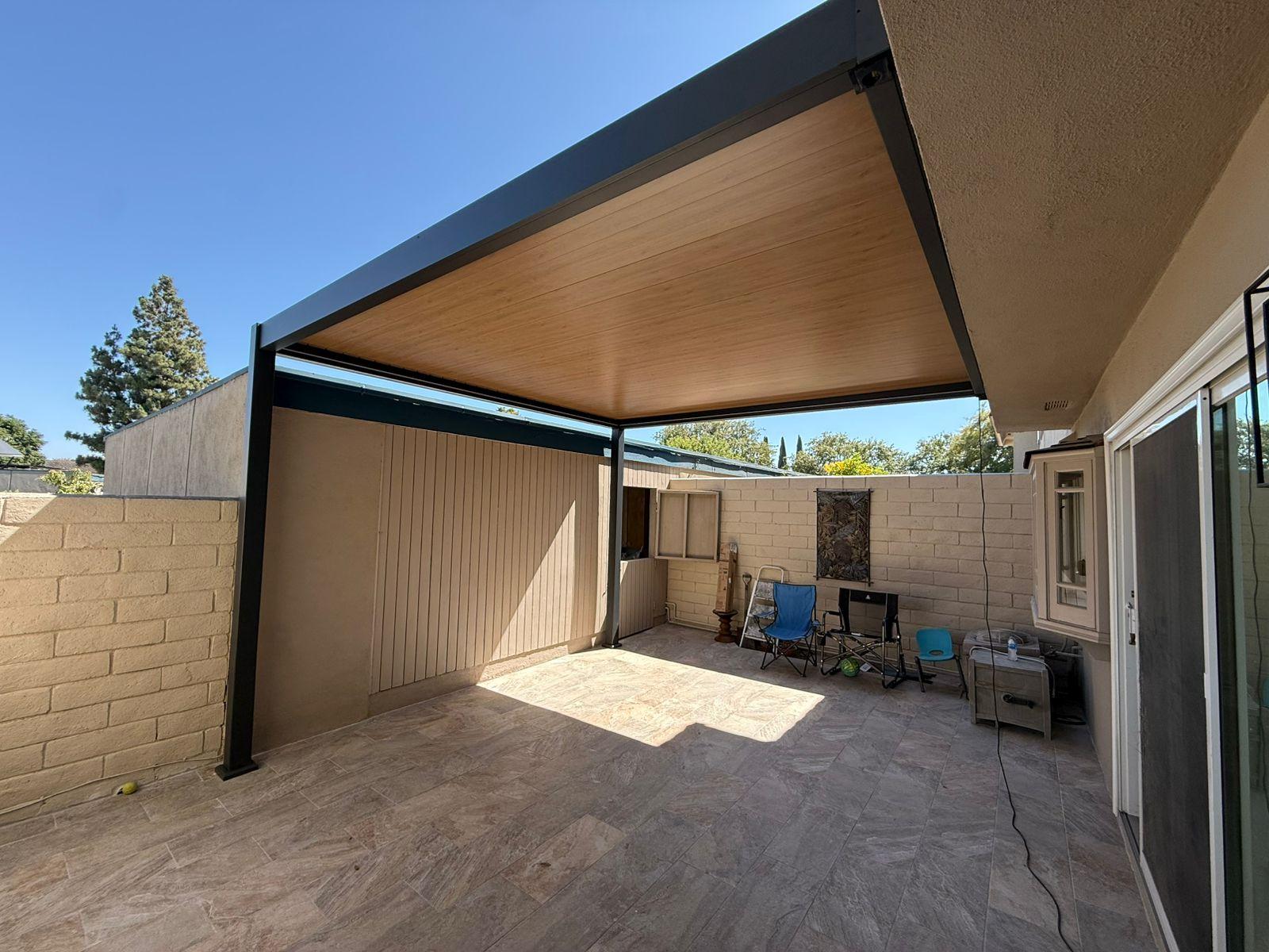 BON Pergola Villa Pergola in dark gray with oak grain louvers, wall mounted over a tiled patio