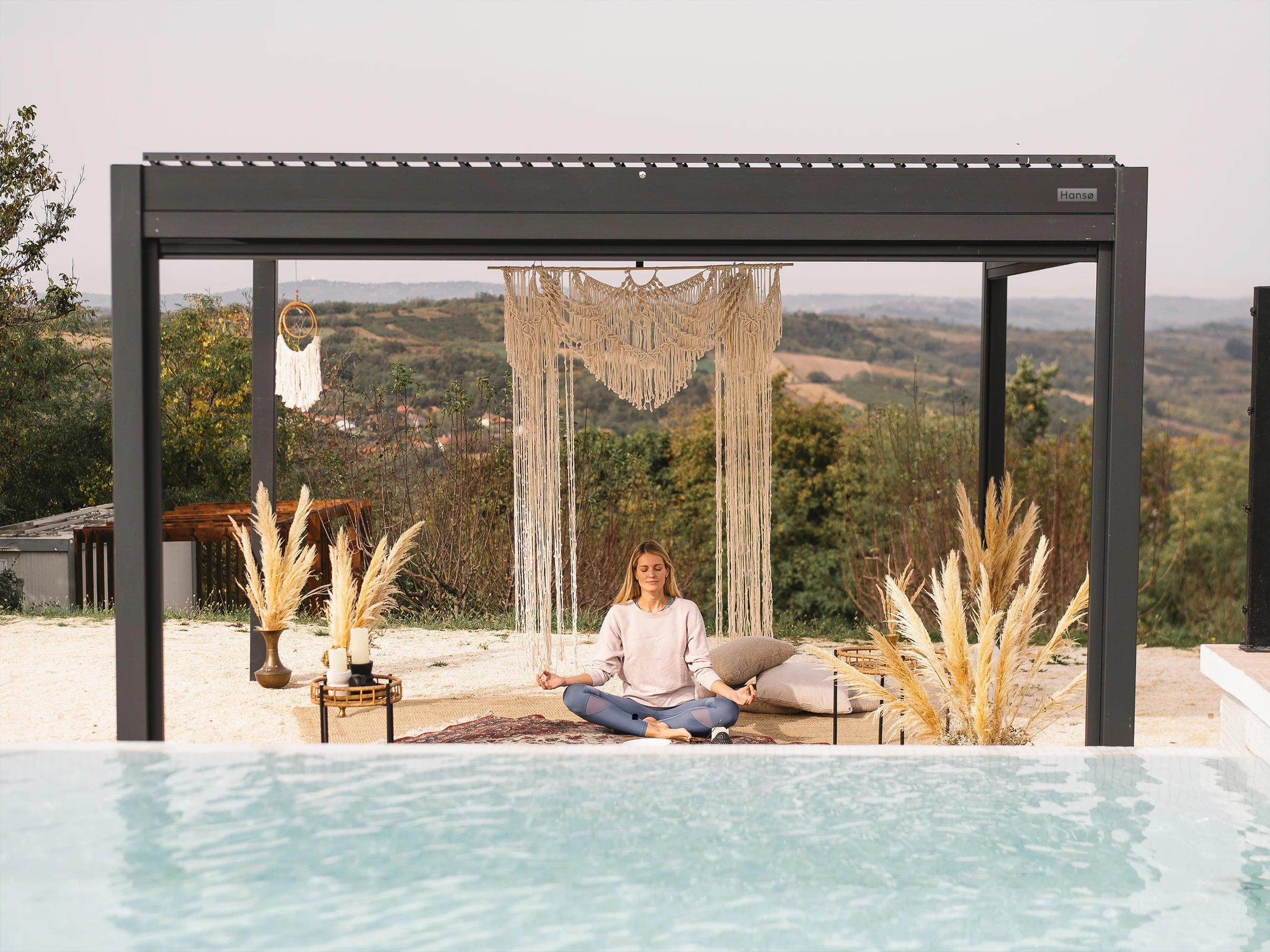 Hansø Pro+ pergola with a dark gray aluminum frame over a lounge seating area, louvers open, hillside beyond