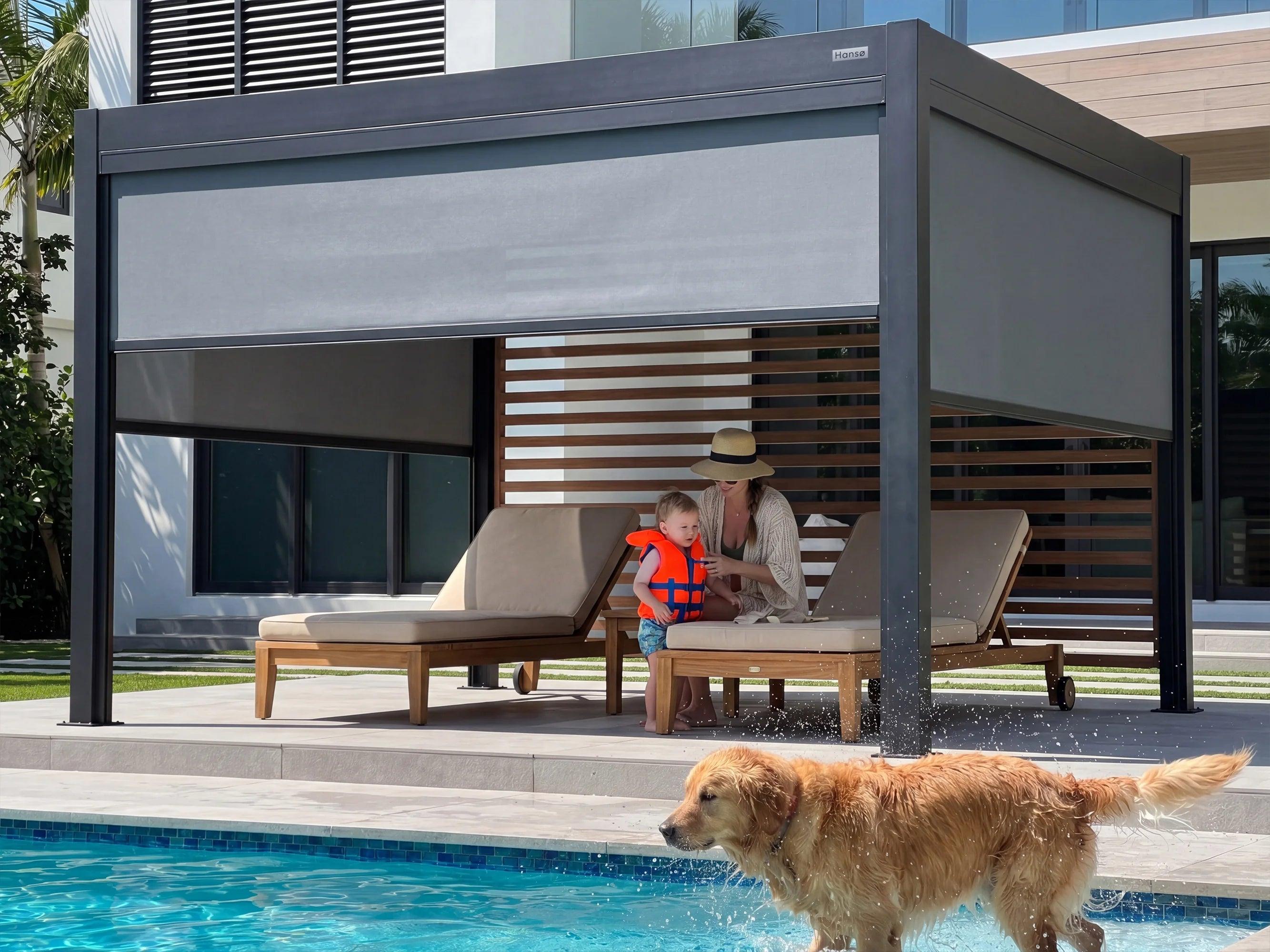 Hansø Pro+ pergola in dark gray beside a swimming pool with sun loungers underneath and a dog on the deck