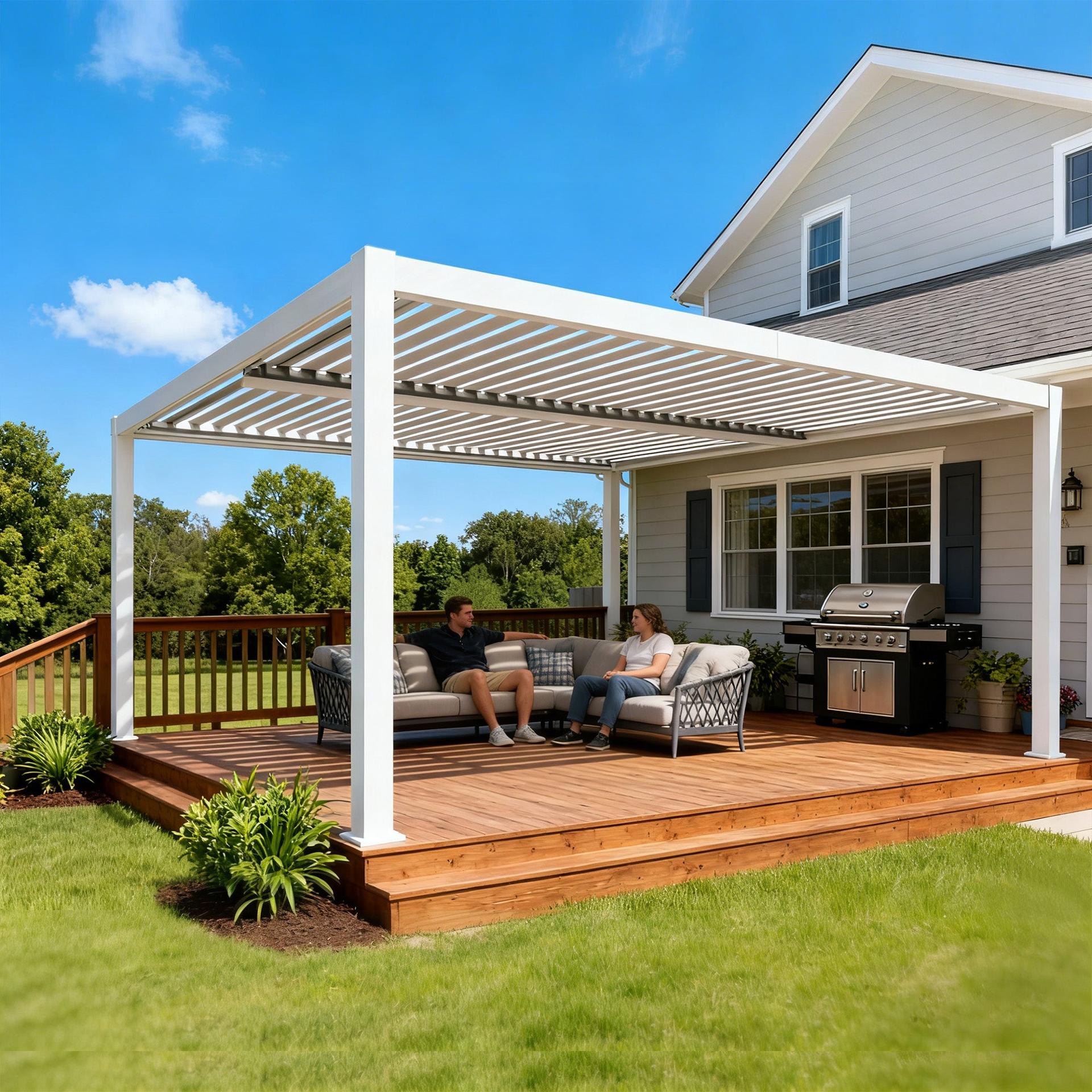 Kozyard white aluminum louvered pergola on a wood deck beside a house, with outdoor seating and a grill