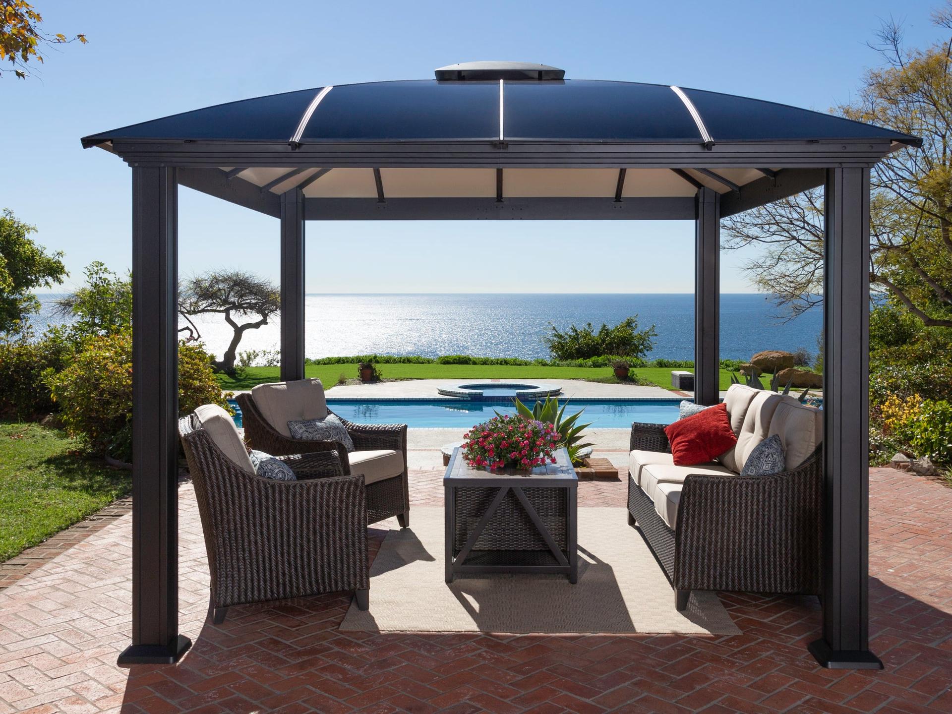 Paragon Cambridge dark aluminum hard top gazebo with a domed roof over wicker seating beside a pool