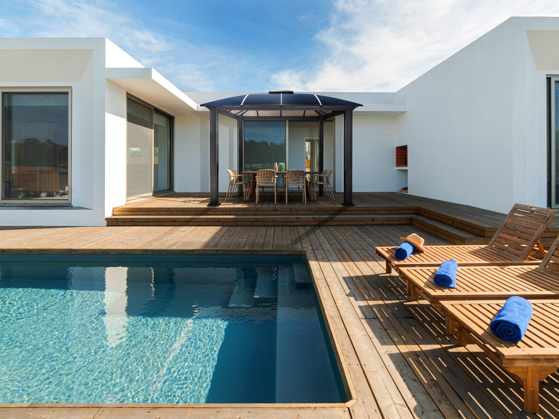 Cambridge hard top gazebo beside a pool deck with a modern house behind