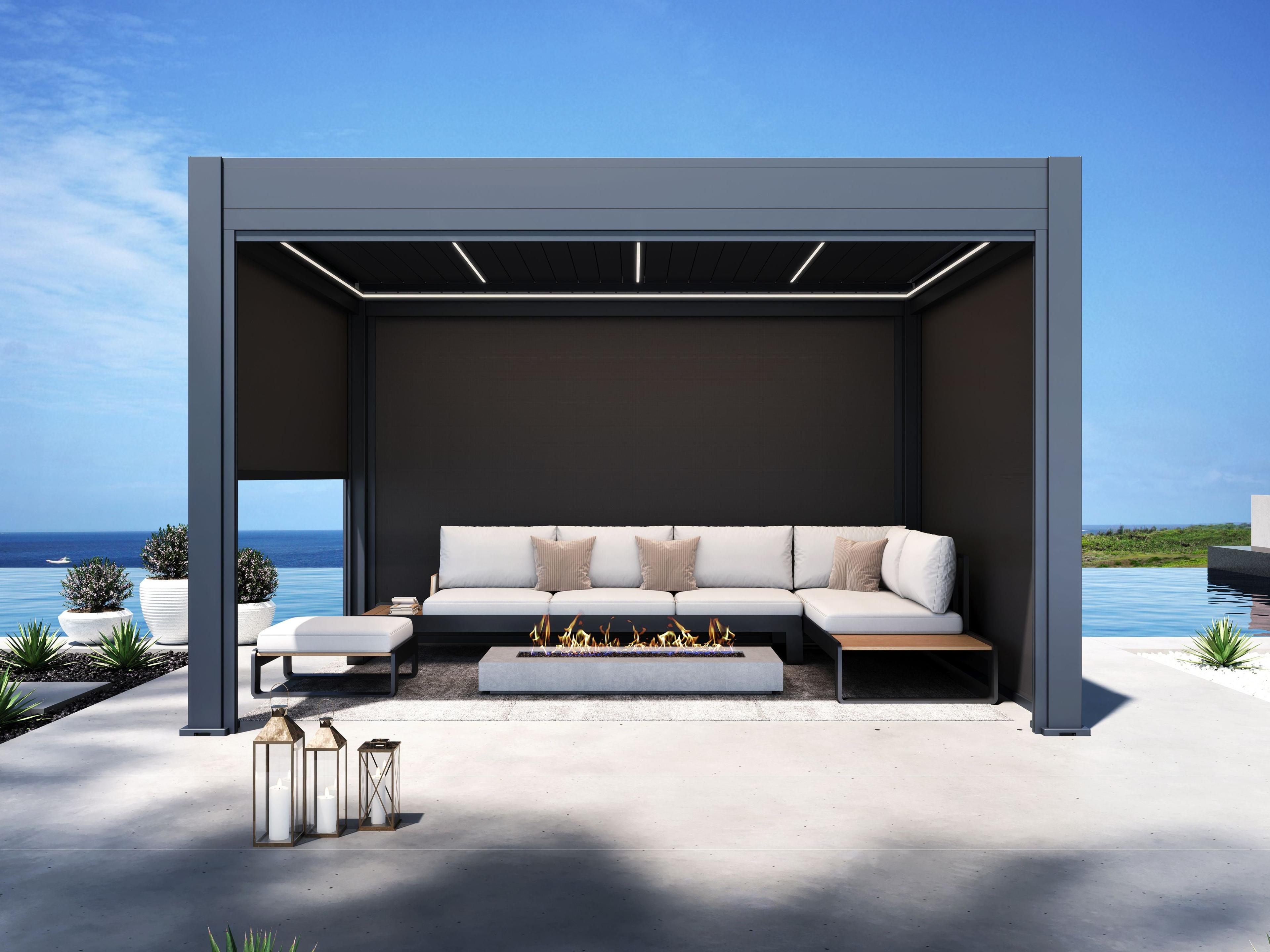 Signature louvered pergola with side screens drawn, sheltering a sofa and fire table on a clifftop terrace above the sea