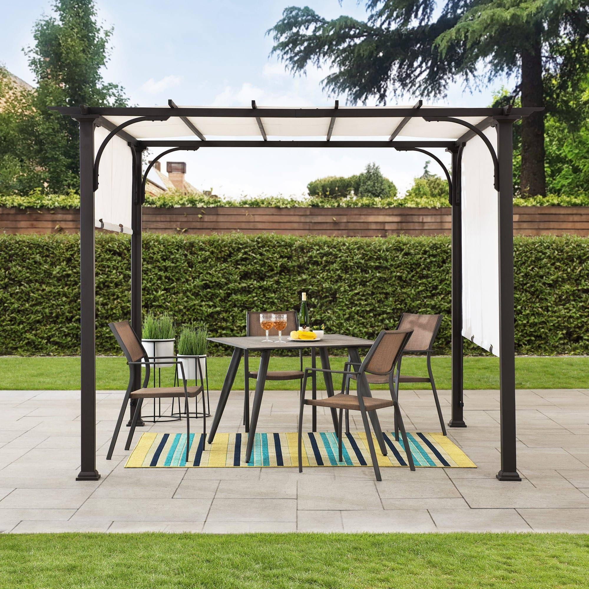 Sunjoy 10x10 white-canopy pergola on a paved patio over a four-seat dining set beside a clipped hedge