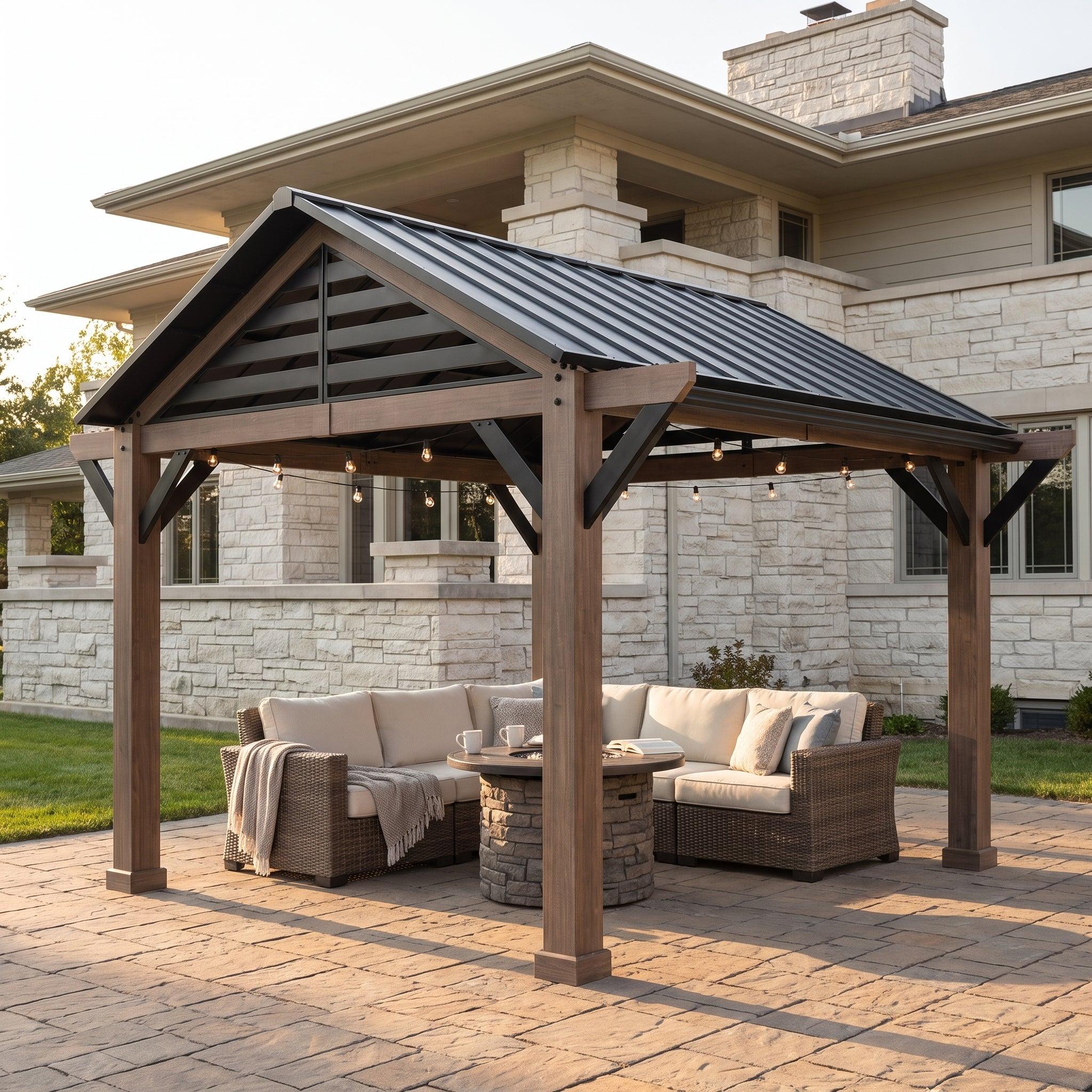 Sunjoy Apex 13x13 gazebo on a paved patio beside a stone house, sheltering a corner sofa and fire table under string lights