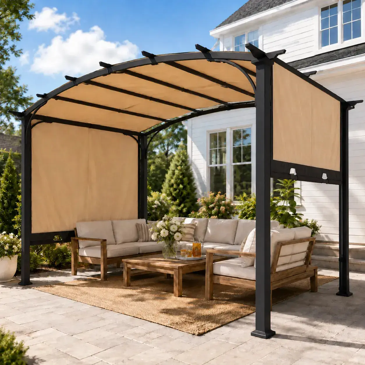 Sunjoy Arcadia Adjustable Arched pergola on a paved patio beside a white house, shading a cream outdoor sofa set