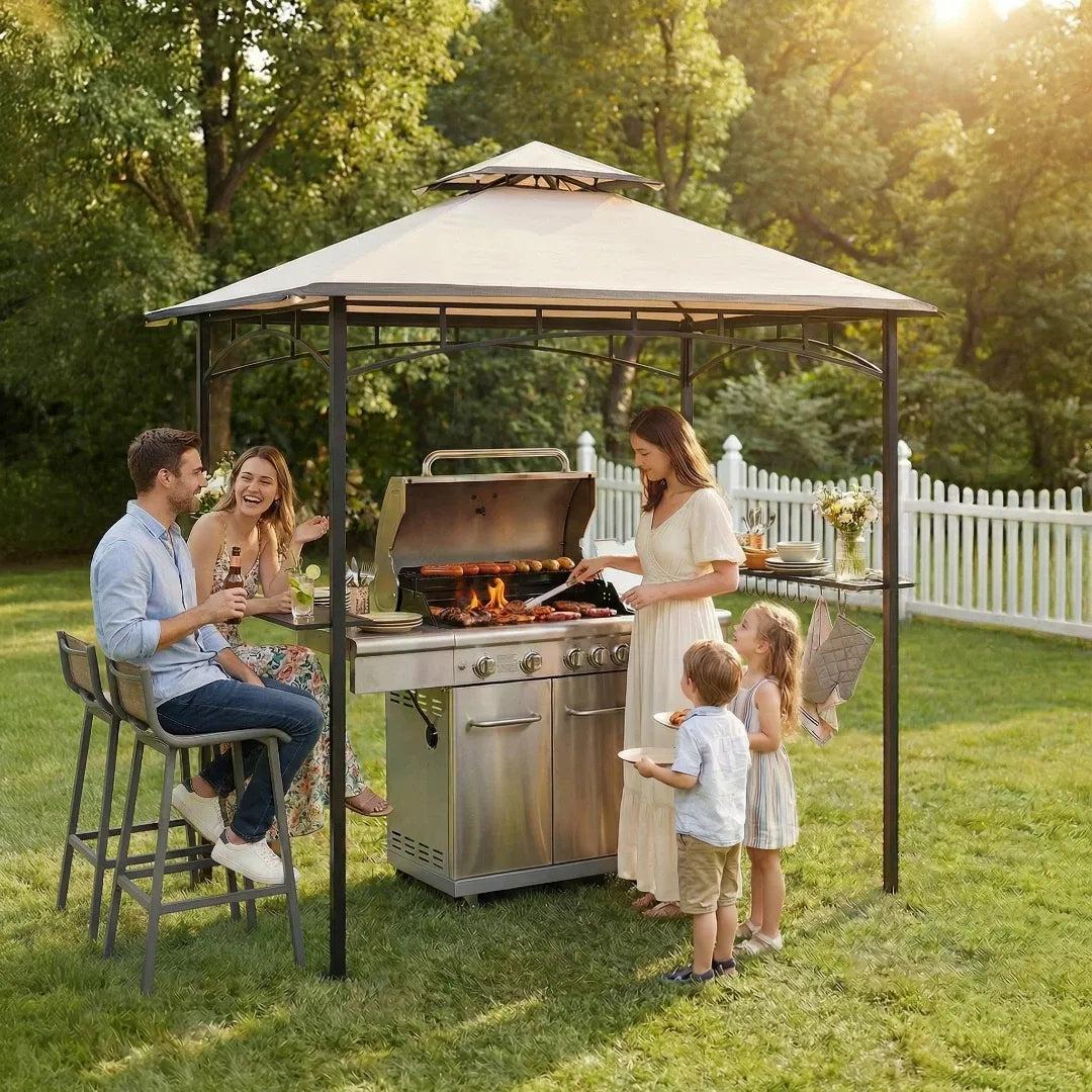Sunjoy BBQ 2-Tier Grill Canopy 5x8 on a lawn, a family gathered around a gas grill sheltered beneath the beige canopy