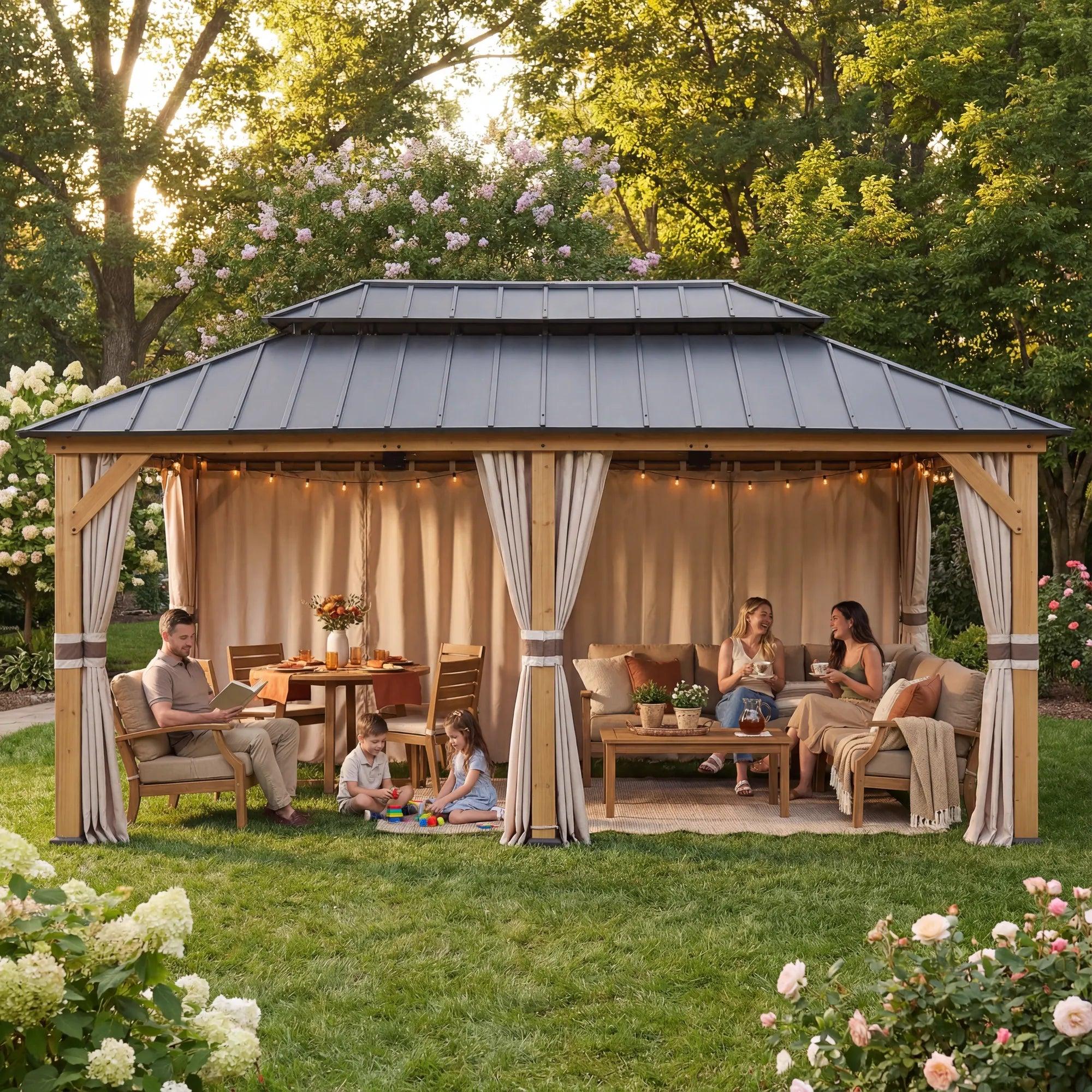 Sunjoy Cedar Wood Gazebo 12×16 on a lawn, honey-toned timber posts and beam under a two-tier grey galvanized steel roof, beige curtains tied at each post and string lights over a dining table and sofa