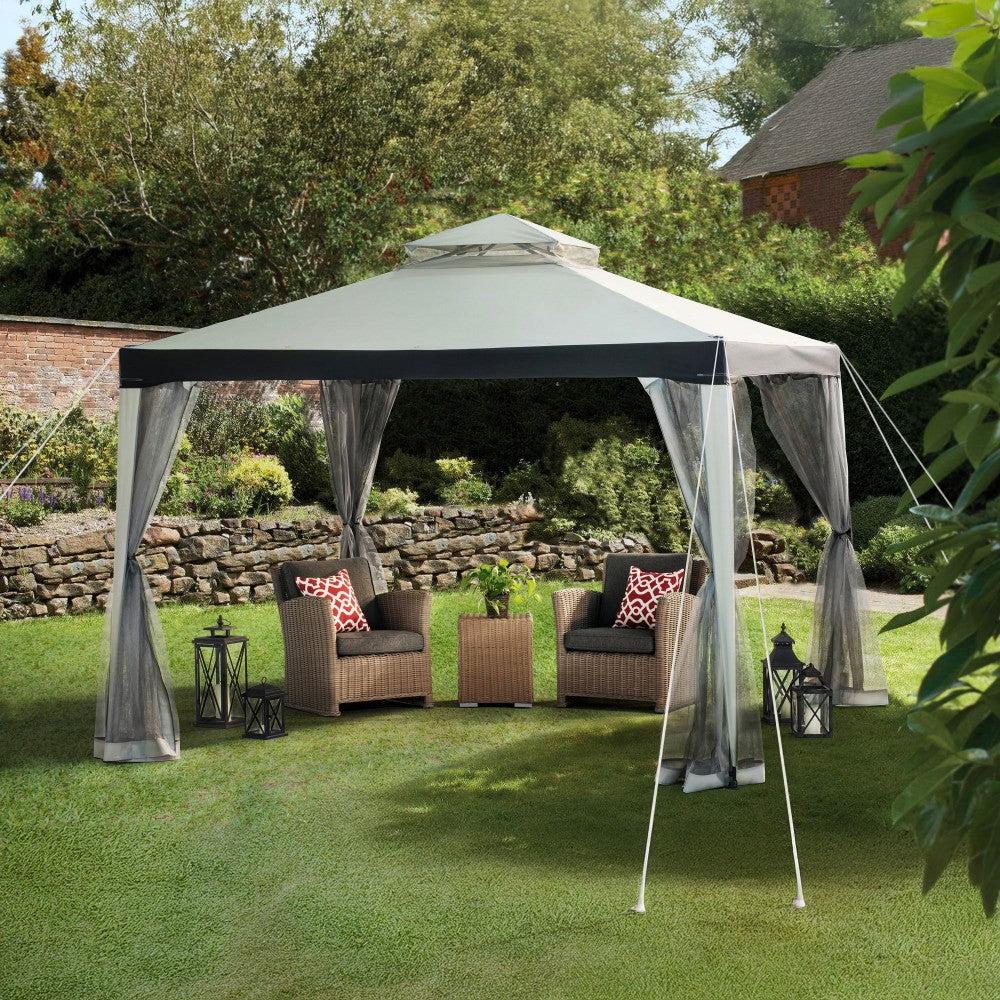 Sunjoy Chatam 10x10 soft top gazebo on a lawn with garden chairs and a side table beneath the canopy