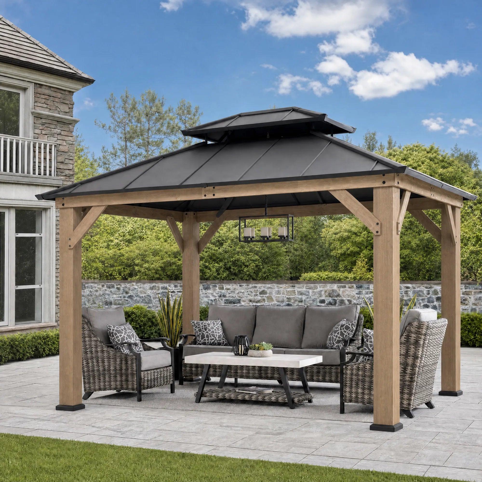 Sunjoy Double-Tier Cedar 10x12 gazebo on a patio beside a stone wall, sheltering rattan sofas around a low table