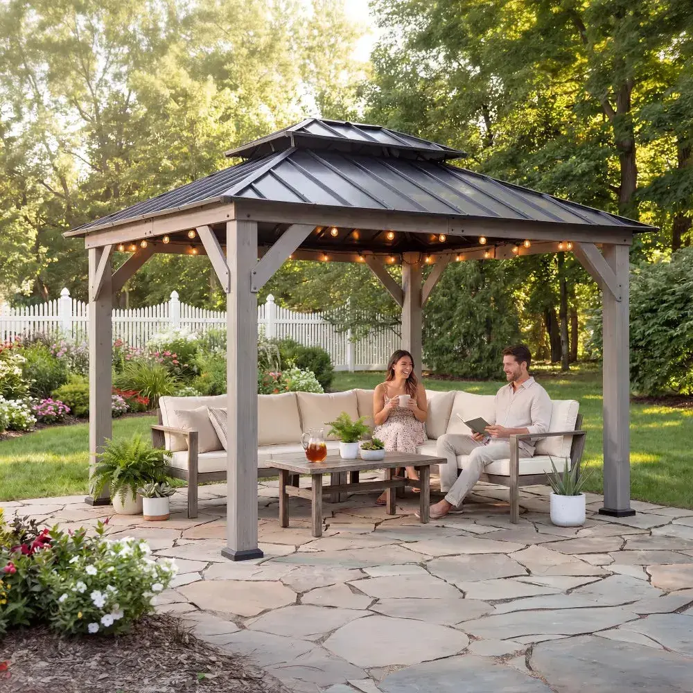 Sunjoy double-tier cedar 10×12 gazebo in driftwood grey with a two-tier steel hardtop roof and string lights over a sectional sofa and coffee table on a stone patio