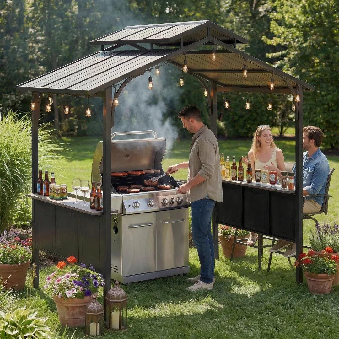 Sunjoy Hanscom 5x8 hardtop grill gazebo in a garden with string lights, a man cooking at a gas grill and guests seated alongside
