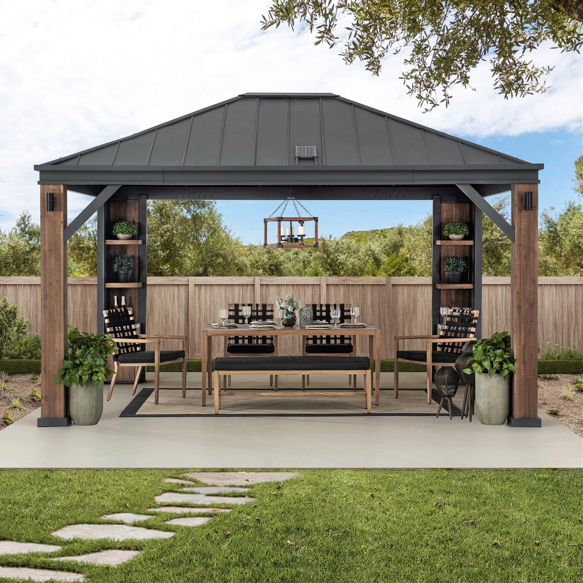 Sunjoy Solaria Smart Tech 12x14 gazebo on a lawn beside a fence, sheltering a long dining table with the corner cabinets stocked