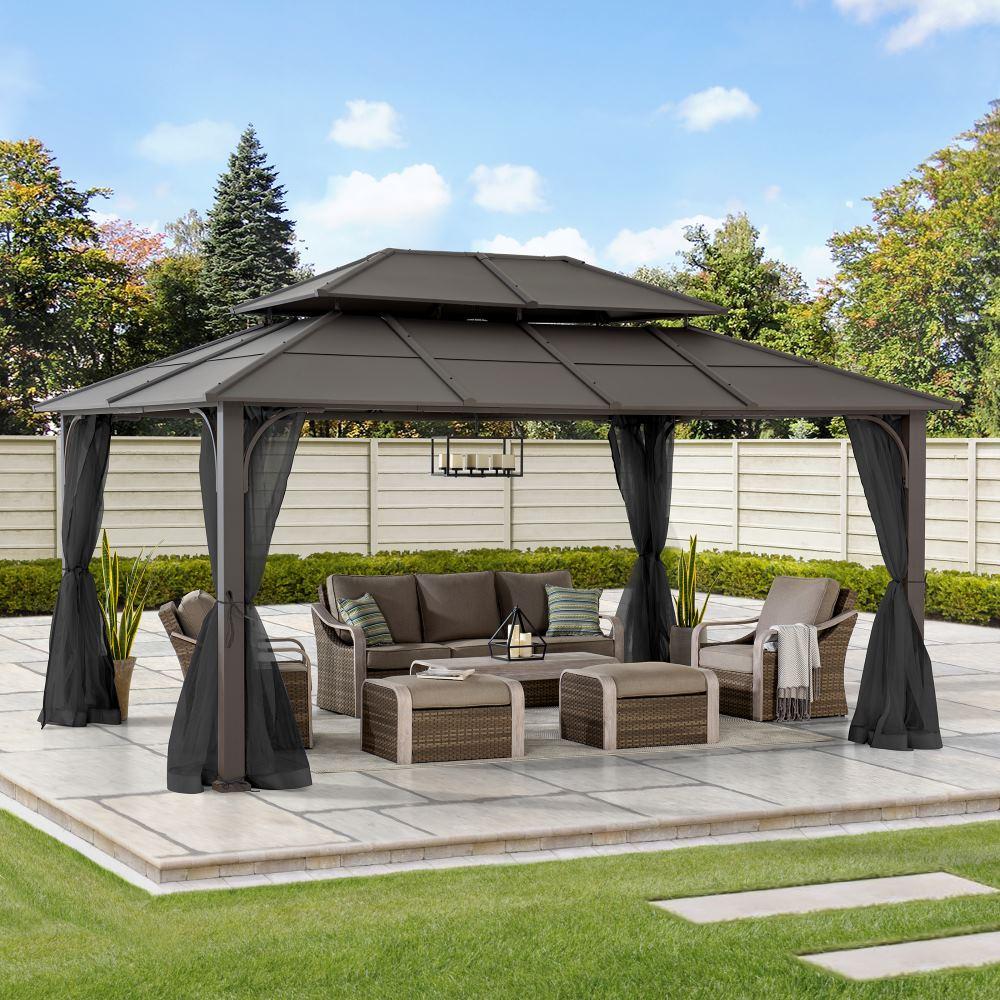 Sunjoy Summit Classic 12x16 gazebo on a paved patio, sheltering a wicker sofa, armchairs and ottomans with a candle chandelier hung from the ceiling hook
