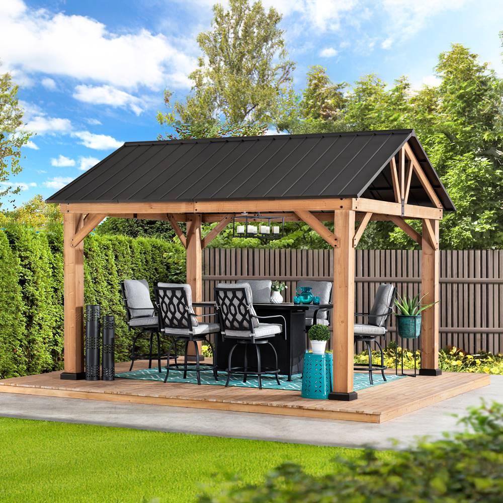 Sunjoy 11x13 wooden-frame gable roof gazebo on a lawn beside a fence, sheltering a bar table and stools