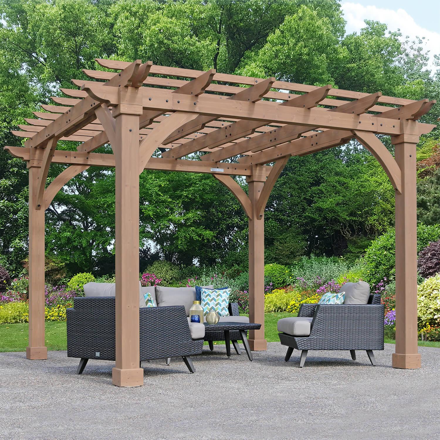 Yardistry 12 x 12 Pergola in stained wood with crisscross trellis joists and curved gussets, over a rattan lounge set on a gravel patio