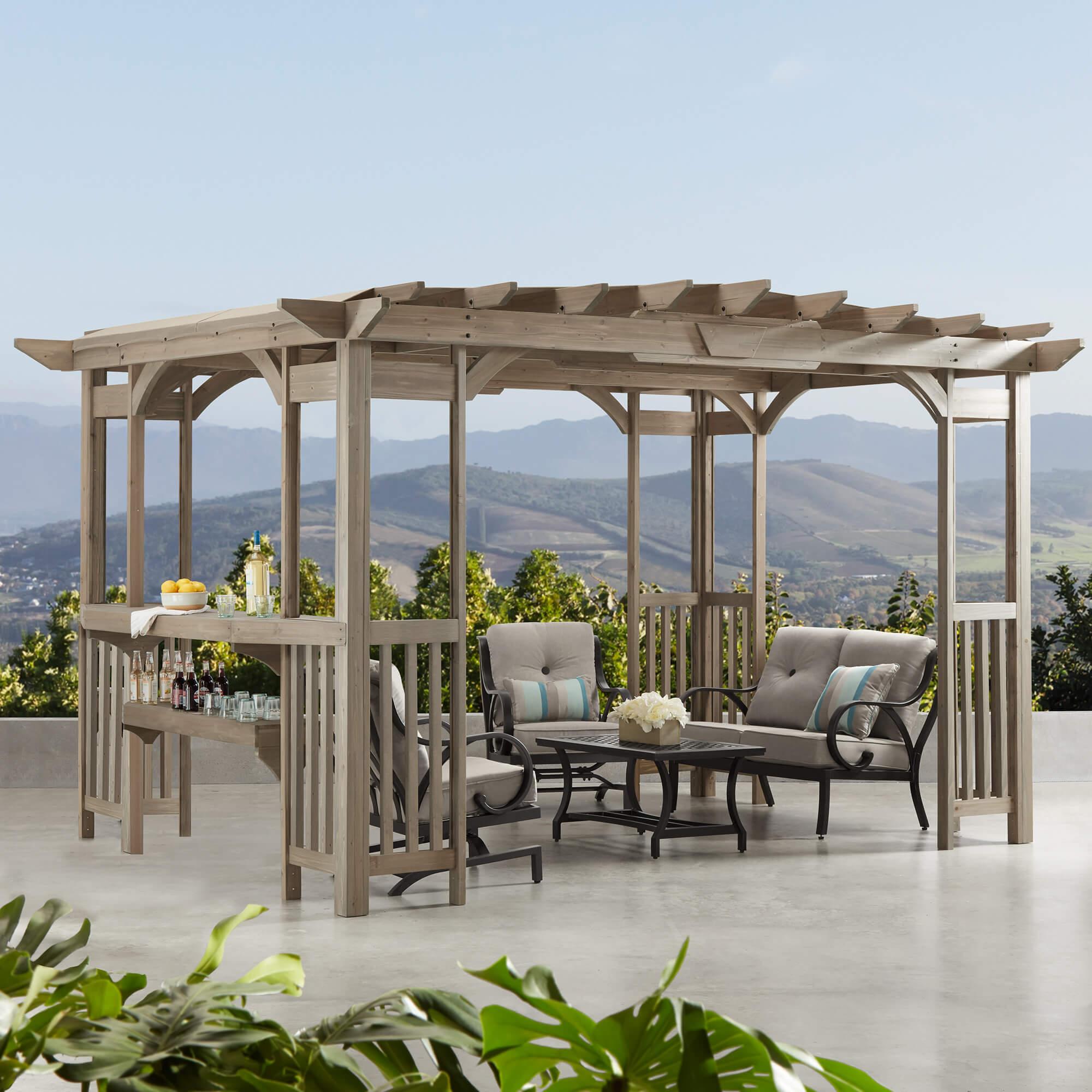 Yardistry Madison Pergola in Timber Grey stained cedar with its bar and counter feature, on a concrete terrace overlooking rolling hills
