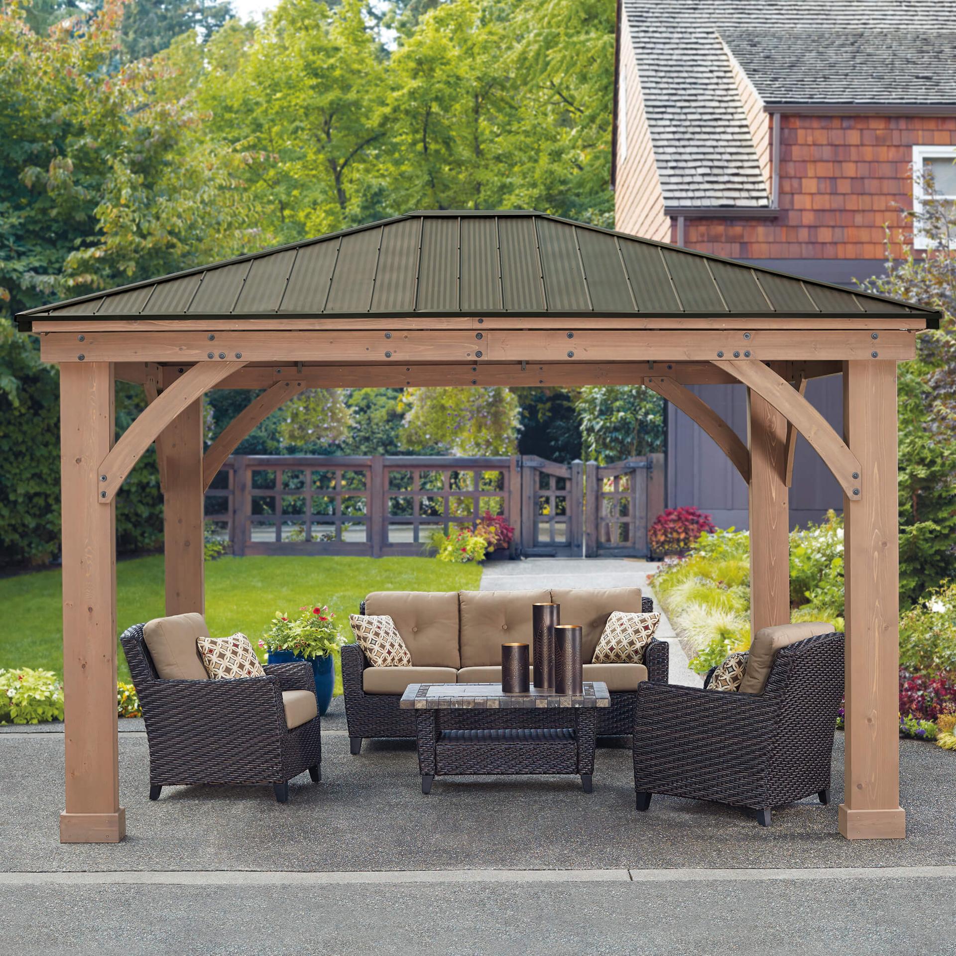 Yardistry 12x14 wood gazebo with a Montana bronze aluminum roof over outdoor sofa seating beside a brick house