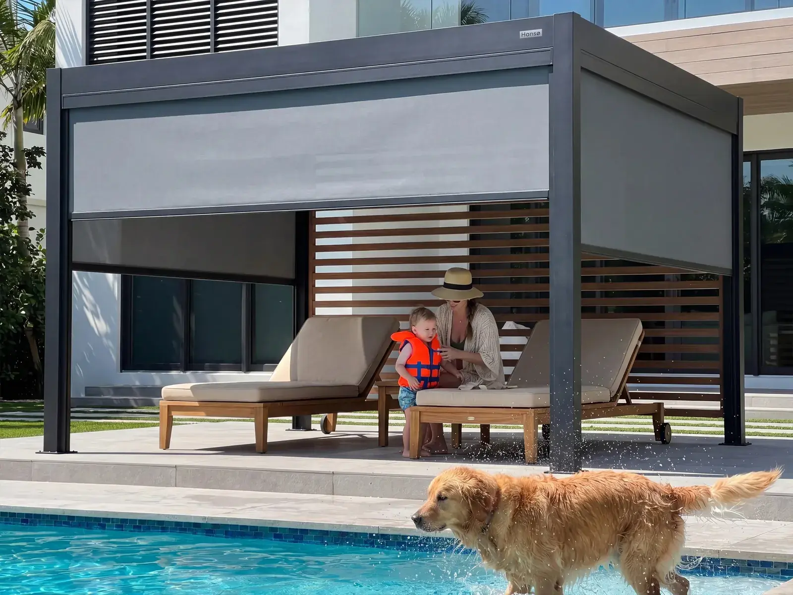 Hansø Pro+ pergola in dark gray beside a swimming pool with sun loungers underneath and a dog on the deck
