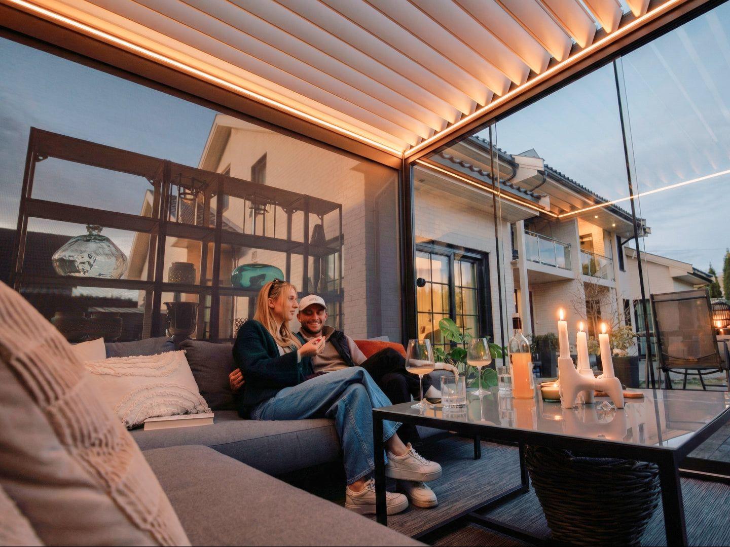 Woman using the remote control under a PERGOLUX Pergola 4 Pro motorized louvered pergola in anthracite on a garden terrace
